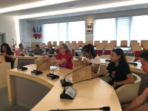 Students sitting on white chairs in a conference room and opening gift bags.