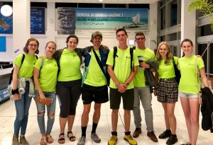Group of eight people standing and wearing bright green shirts at the airport terminal in New Caledonia