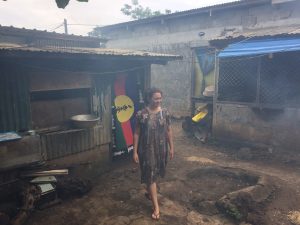 One woman wearing islander dress walking in a village with some smoke from fire