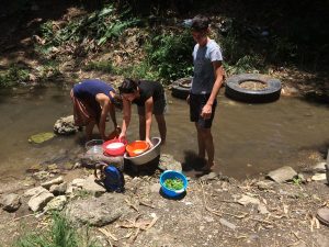 Three people with their feet in a creek washing the dishes