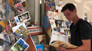 Young caucasian man standing up and reading a book inside the library