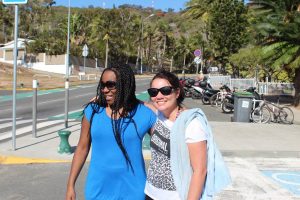 Two women wearing sunglasses and holding each other posing for a photo on the side of the road