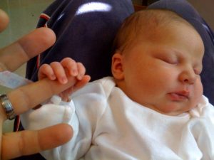 A baby holding the finger of an adult.