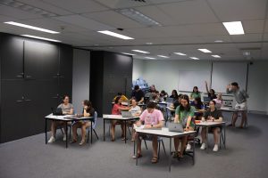 Sixteen Students shown in a classroom. Students are sitting in pairs with laptop devices on the desks.