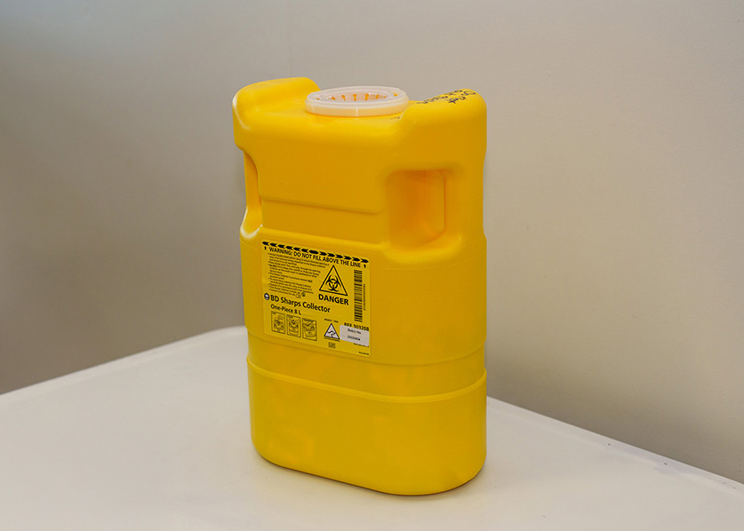 Photo of a yellow sharps disposable container on a desk.