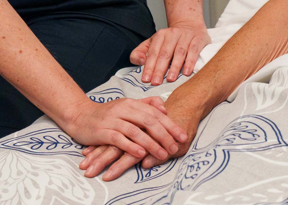 Close-up photo of a nurse's hands holding a patient's hand.