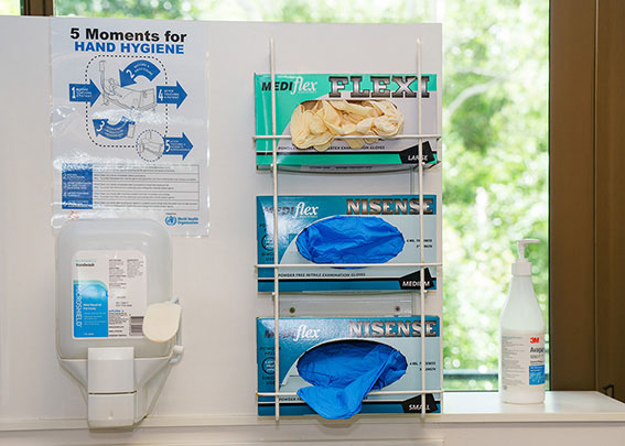 Three boxes of gloves stacked on a rack by the hand soap dispenser, hand sanitiser, and a handwashing poster.