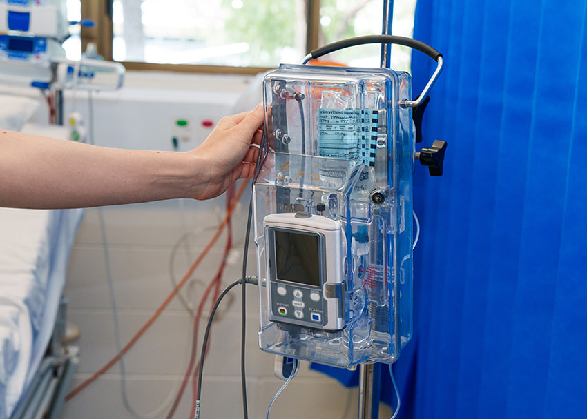 A cropped photo of a hand reaching for a PCA pump in a hospital room.