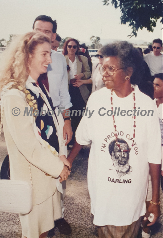 Anita Keating stands beside (and holds the hand of) Bonita Mabo, who wears a shirt with Eddie Koiki Mabo's face surrounded by the words "I'm proud of you darling"