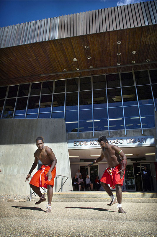 Two Indigenous male dancers performing a dance on the front steps of the Eddie Koiki Mabo Library
