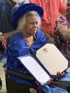 Side view of Bonita, dressed in blue cap and gown, seated and holding her Honorary Doctorate