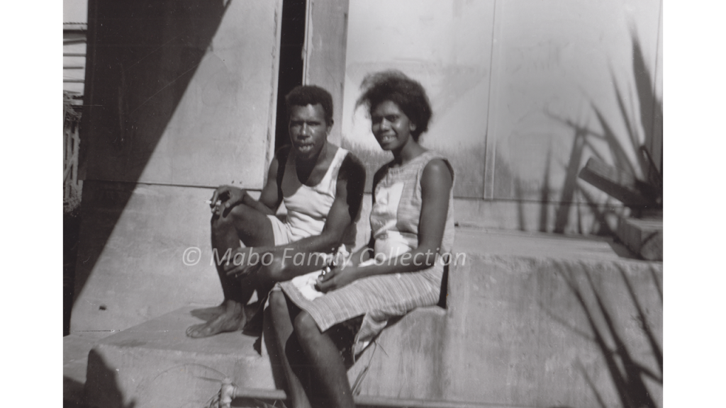 Man and woman in summer clothing, sitting on concrete steps in front of a building.