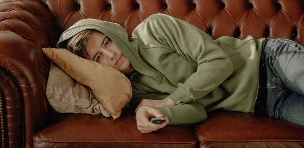 Man lying down on couch wearing a hoodie.