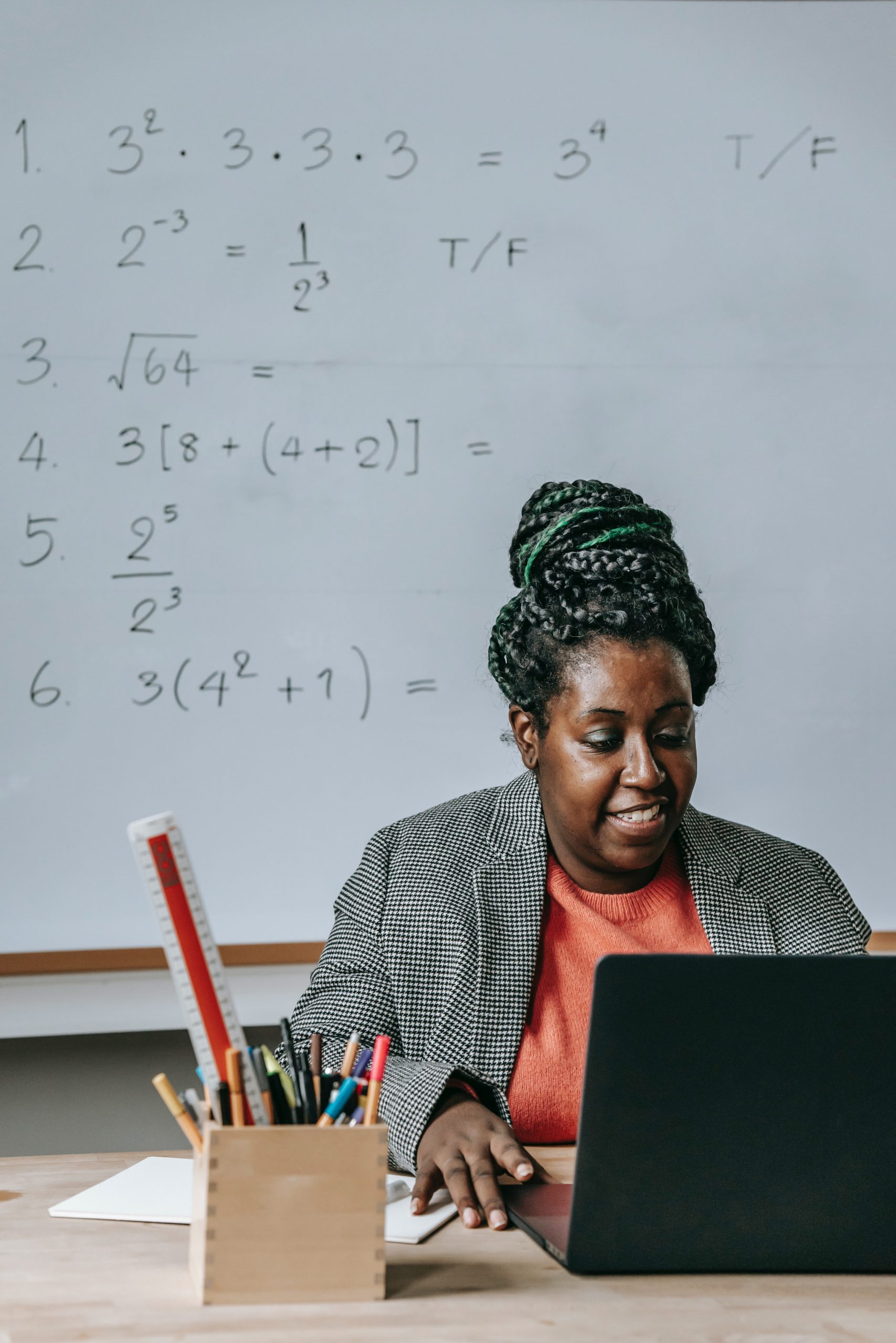 Black woman sitting at desk with laptop with whiteboard of equations behind her