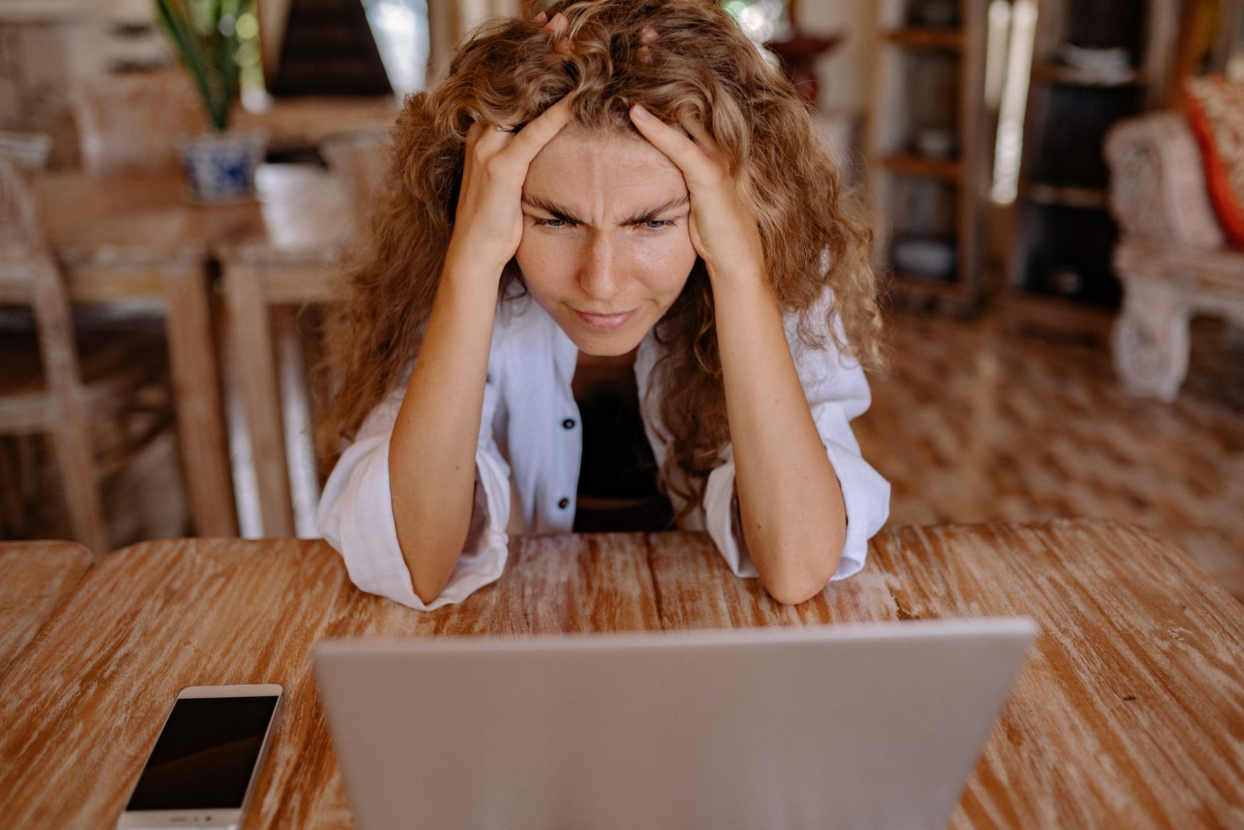 Woman looking at laptop, with hands on head, looking stressed