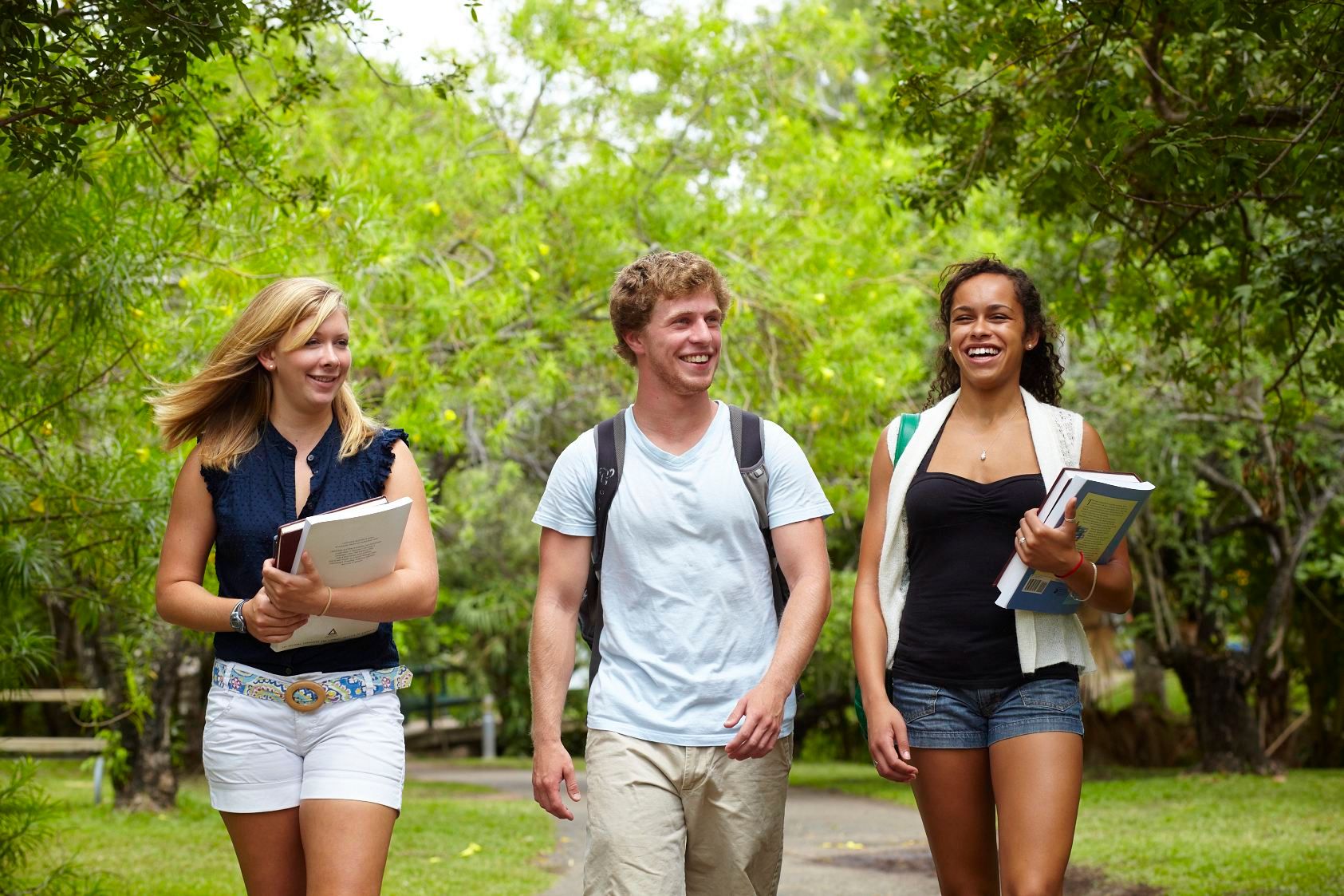 Two women and a man walking, smiling and talking on a green tree filled pathway at James Cook University Library