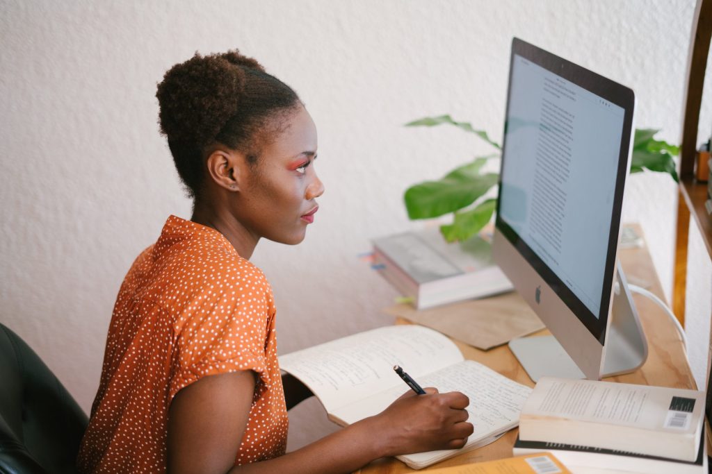 Woman taking notes in a notebook while looking at her desktop computer